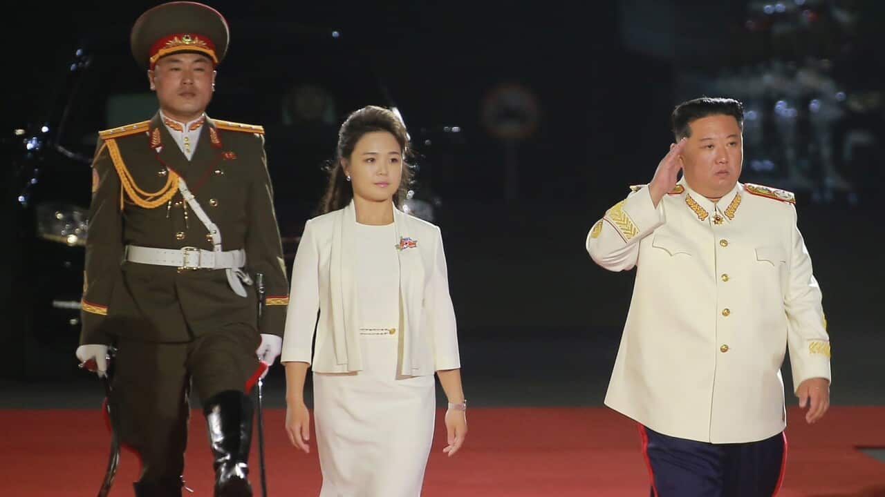 A man, woman and soldier are seen walking down a red carpet.