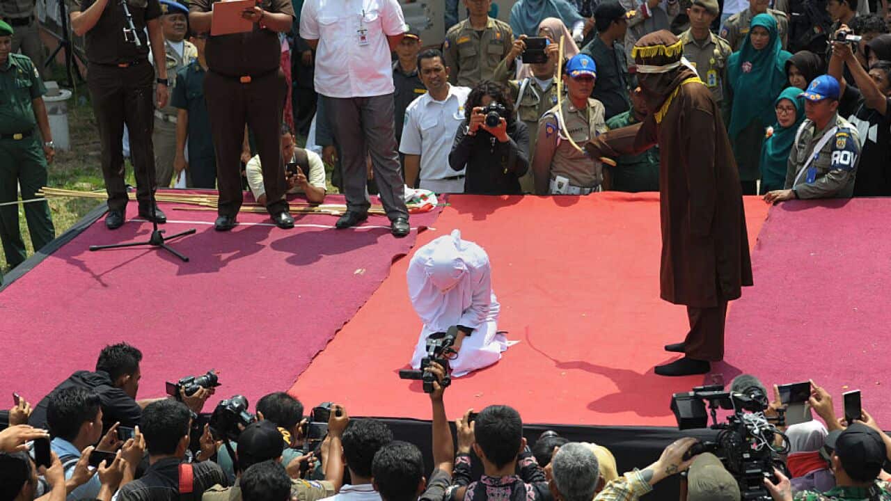 File: A sharia policeman (R) canes a woman (C-kneeling) for breaking Islamic law during a public punishment in Banda Aceh on March 1, 2016.