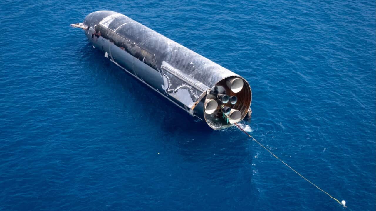 A large rocket floats in water, connected to a long tow rope.