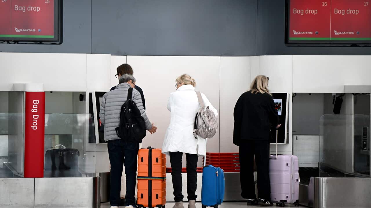 People taking their bags to a bag drop at the airport.