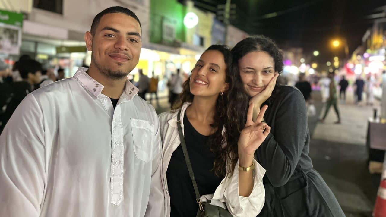 A man and two girls pose on a street at night.
