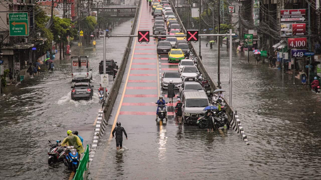 People walk through floodwater on a road during heavy rain in Bangkok