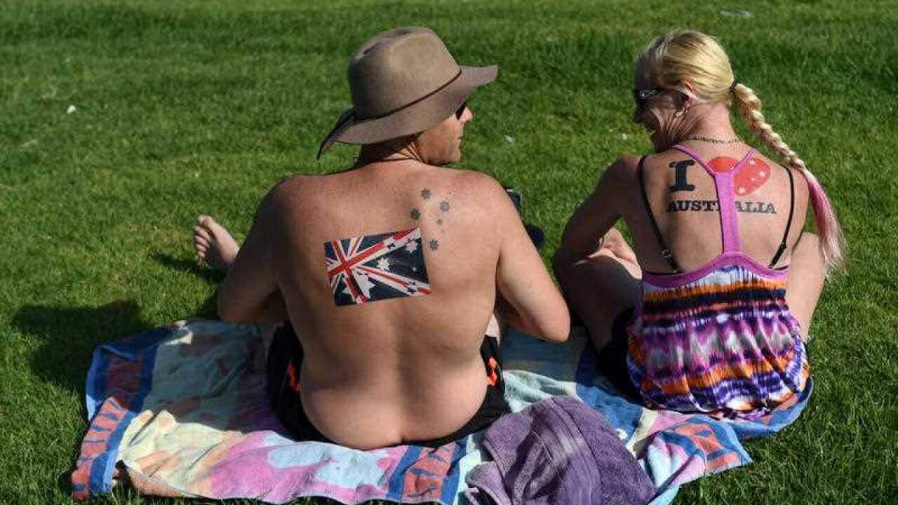 A couple with Australian flag stickers on their backs sit on the grass near Bondi Beach on Australia Day