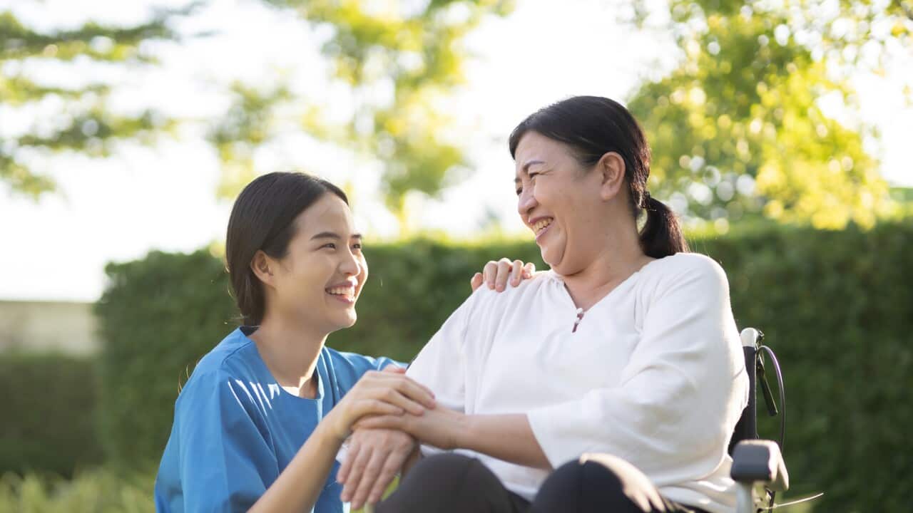 Asian female nurse assisting female senior patient in wheelchair at home