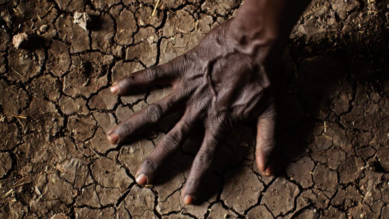 man places his hand on the parched soil in the Sudan