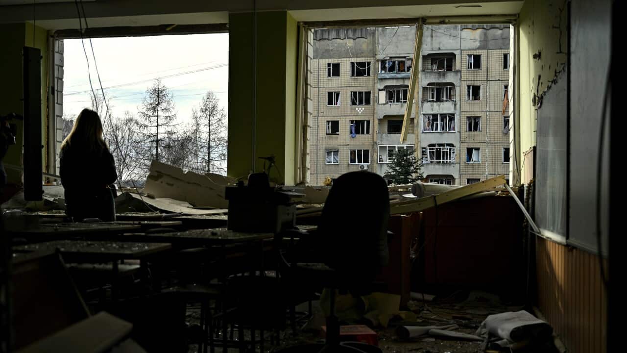 A silhouette of a person staring out a window from a damaged building.