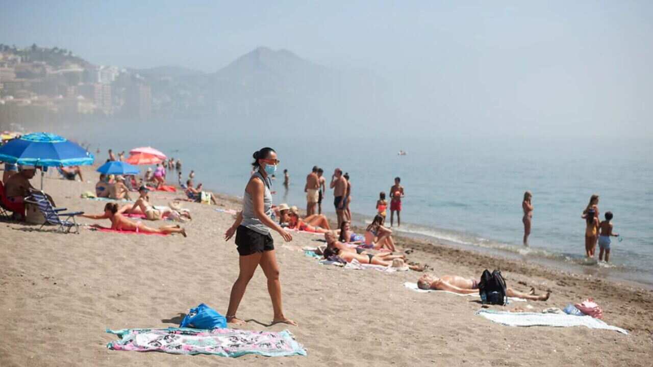 People are seen sunbathing at Malagueta beach, southern Spain, on a foggy day.