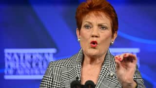 A middle aged woman with red hair speaks into a microphone.