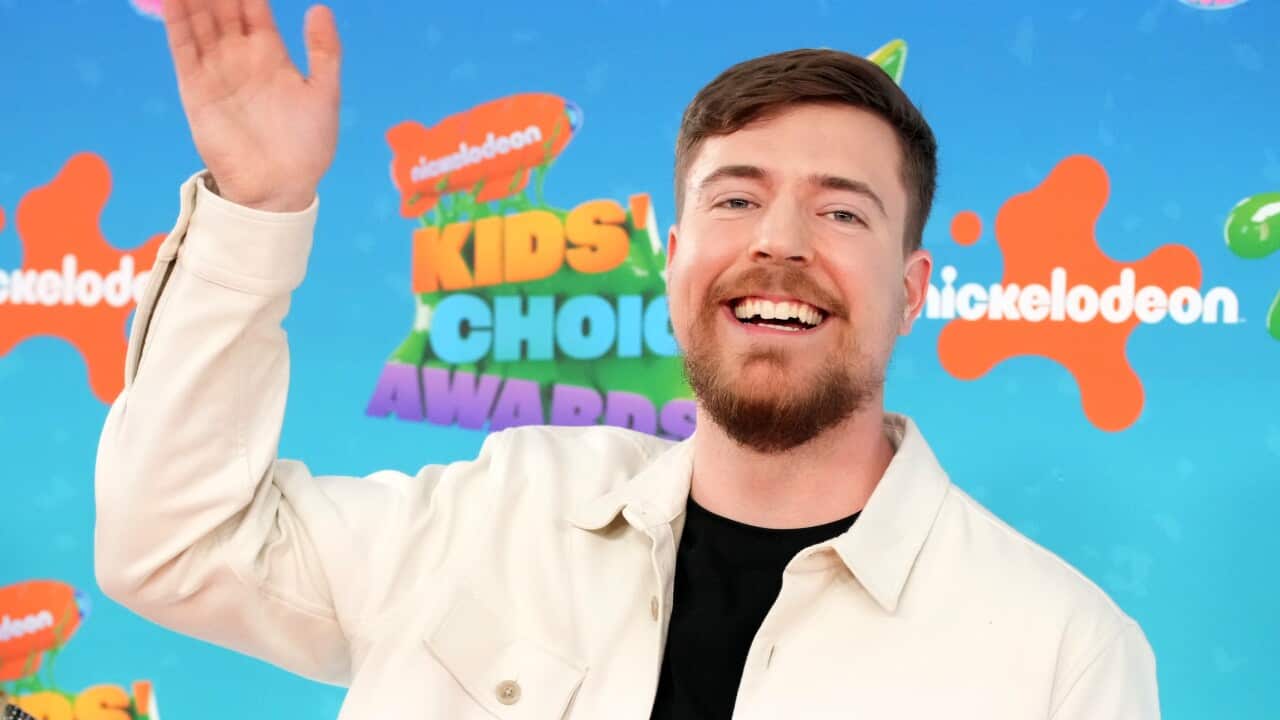 A man in a white jacket smiles in front of a background for the Nickelodeon Kids' Choice Awards.
