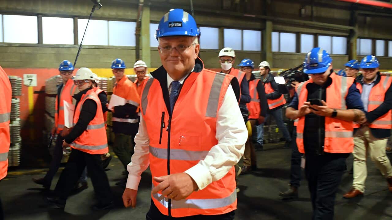 Prime Minister smiles, wearing a hi vis vest and helmet in front of a group of others.