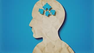 Illustration of a human head silhouette with blue puzzle pieces inside against a blue background.