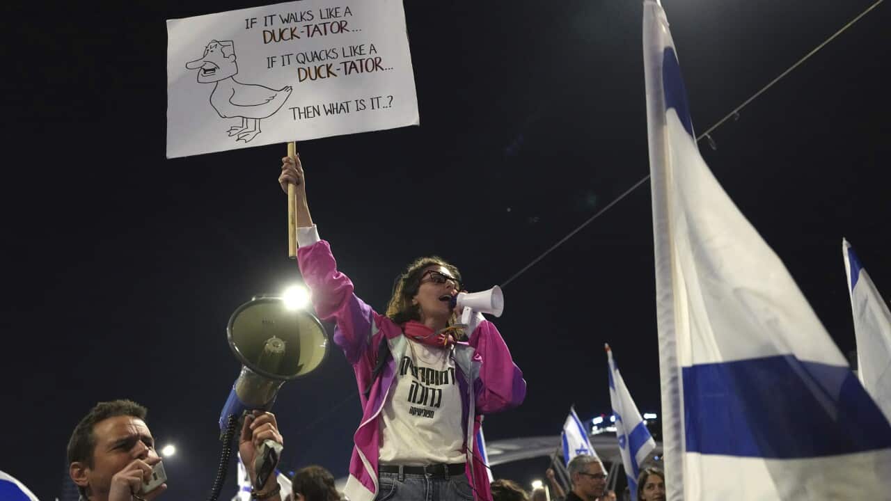 A woman holds a placard and speaks on a megaphone while being surrounded by protestors waving Israeli flags.