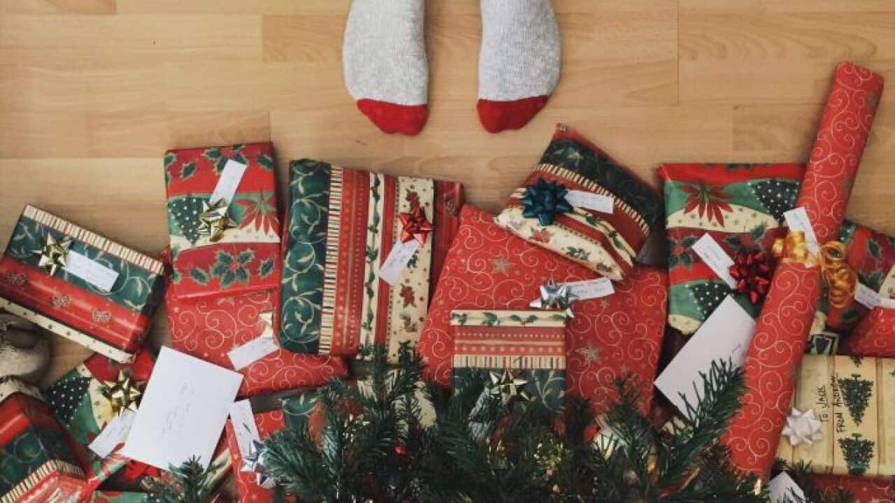 feets in socks underneath christmas tree with many wrapped presents