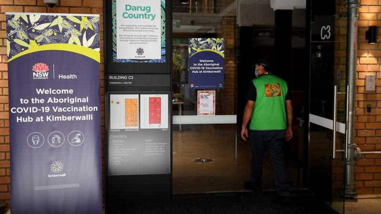A masked person enters a building, with a government sign bidding welcome to the Aboriginal vaccination hub at Kimberwall on Darug Country.