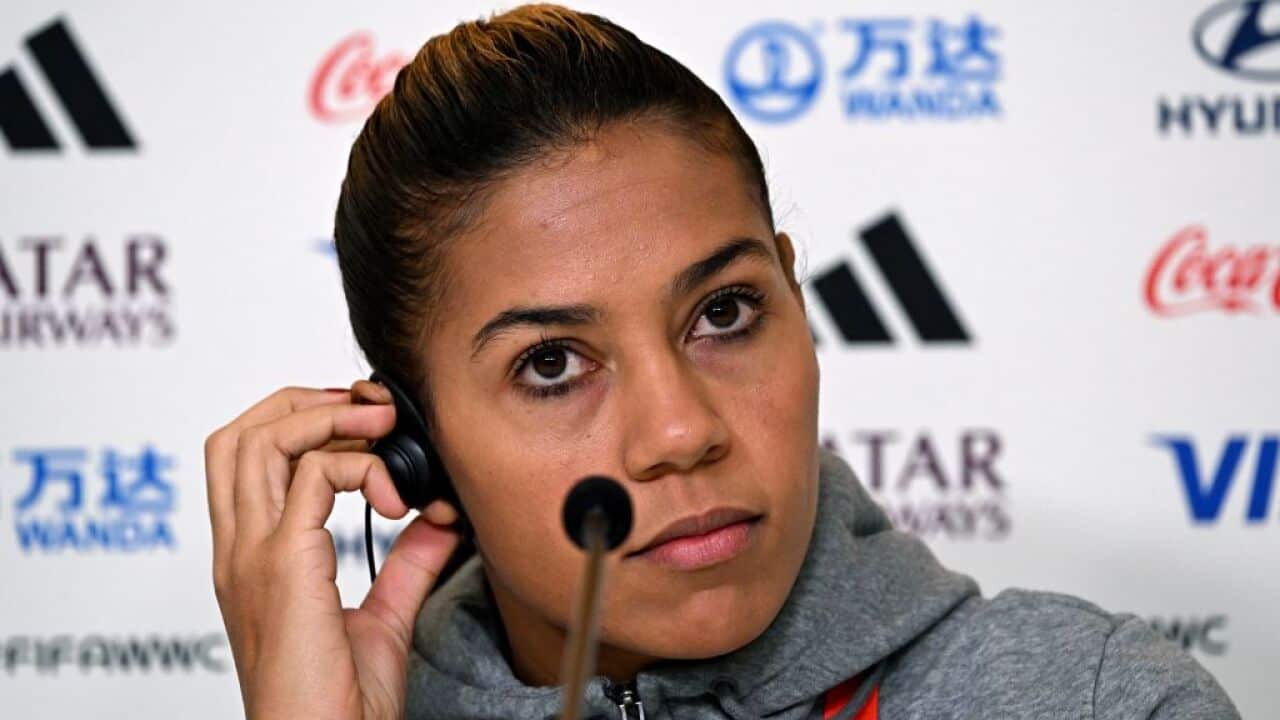 A woman in a grey hoodie holding an earpiece in her ear.