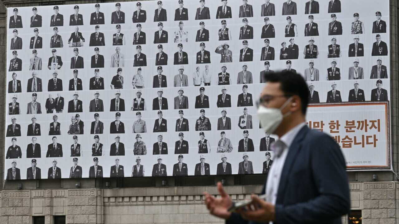 A man walks past a banner showing portraits of Korean War veterans hanging in front of City Hall in Seoul on June 25, 2021, on the 71st anniversary of the outbreak of the Korean War.