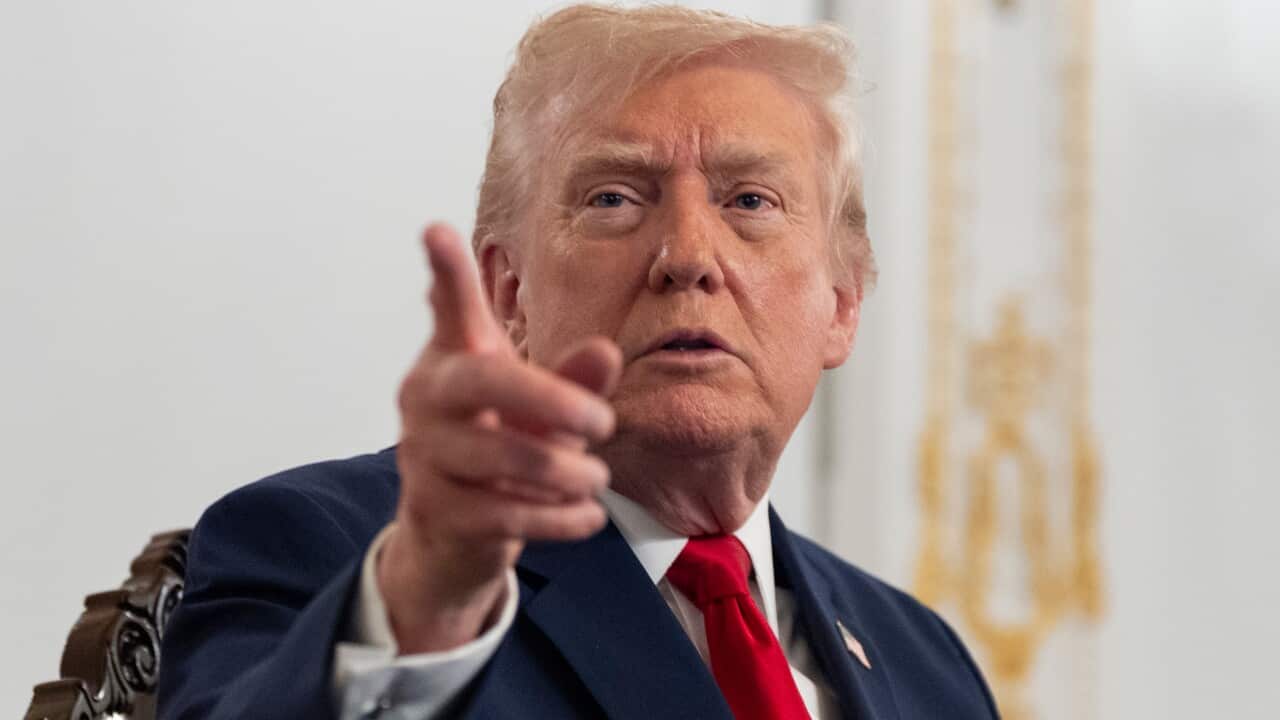 Donald Trump, wearing a dark blue suit and red tie, points his finger