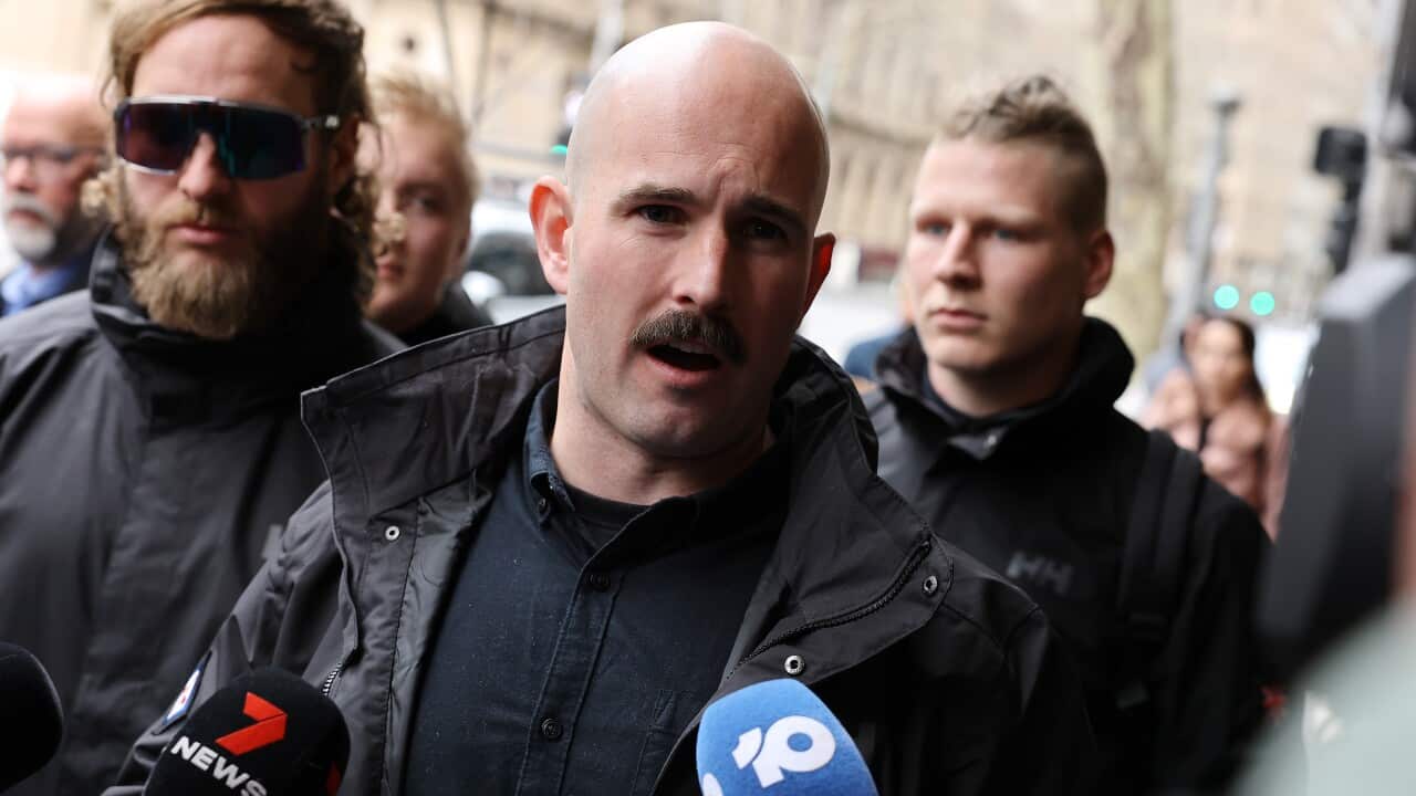 A man with a moustache speaking to microphones