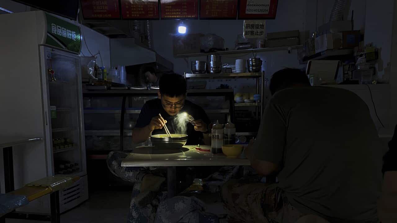A man uses his smartphone flashlight to light up his bowl of noodles as he eats his breakfast at a restaurant during a blackout in Shenyang in northeastern China's Liaoning Province, Wednesday, Sept. 29, 2021. People ate breakfast by flashlight and shopke