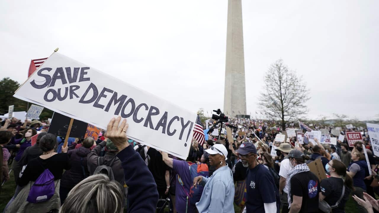 Demonstrators hold up signs during a protest with the Washington Monument seen in the background.