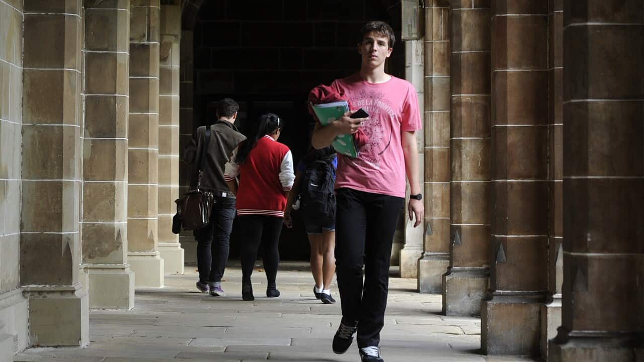 A man in a pink shirt walks the hallway of a university.