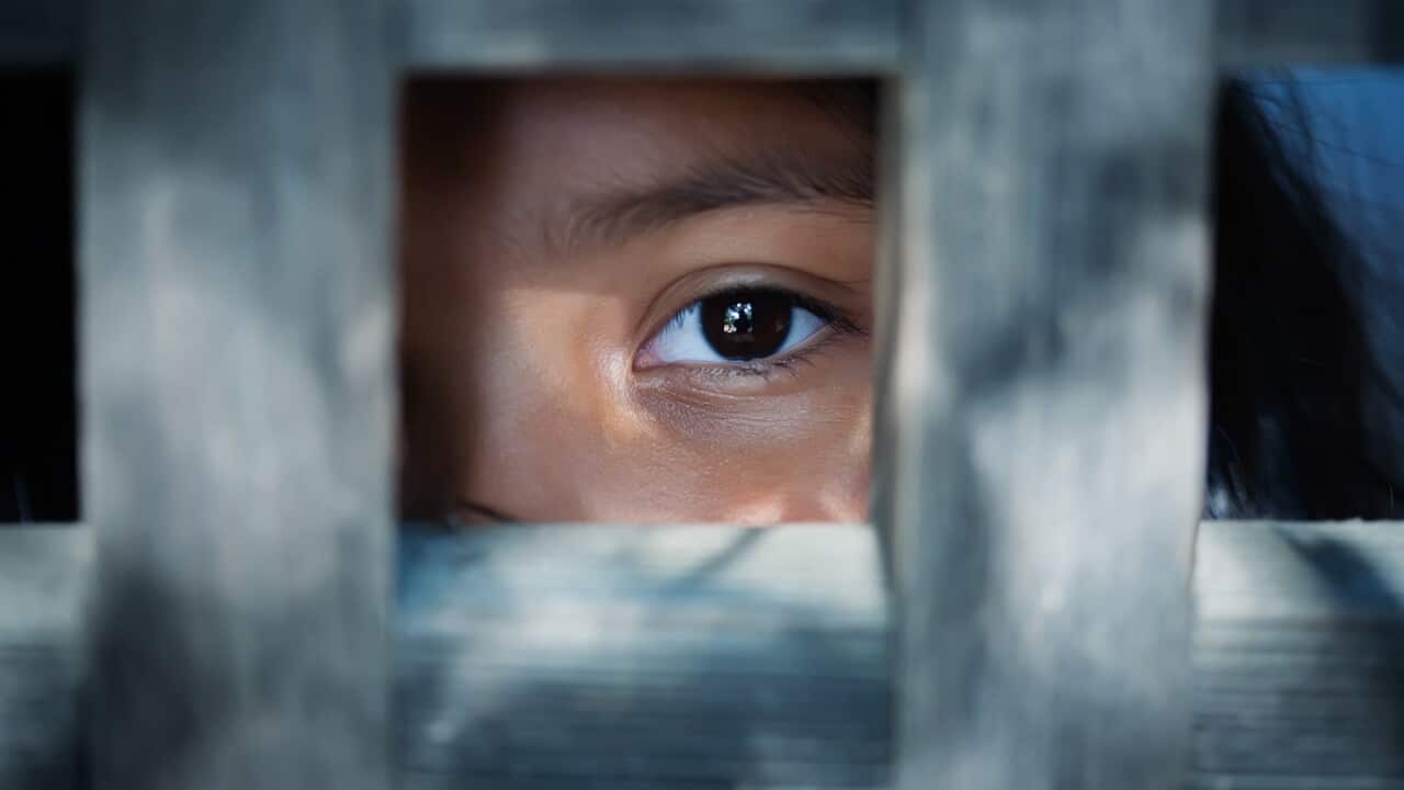 The blank stare of a child's eye who is standing behind what appears to be a wooden frame