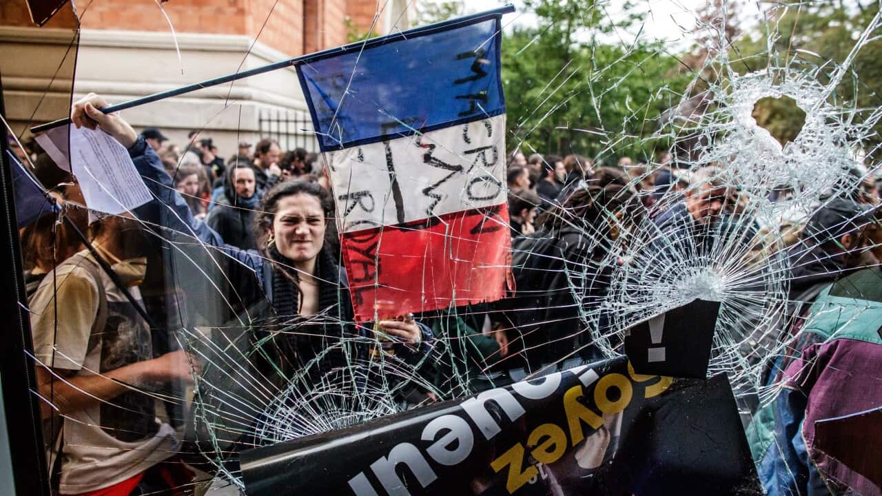 A protester holds a French tricolored flag with an anti-Macron slogan outside a destroyed McDonald's fast food restaurant during a demonstration of workers from the private and public sectors as well as labor unions.
