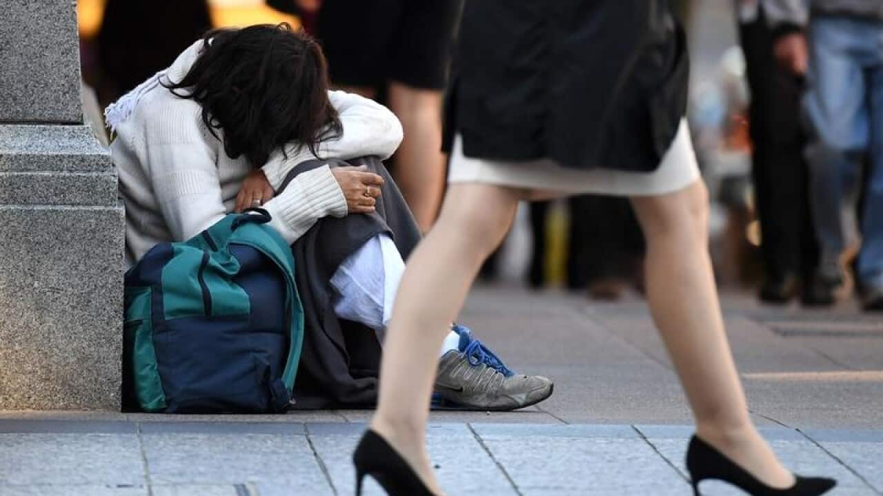 A homeless woman sits on a street corner