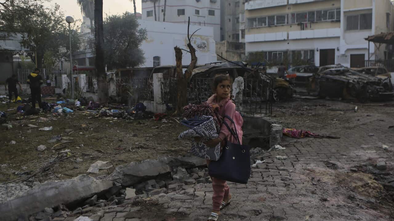 A girl walking past a site where there is debris and burnt-out cars.