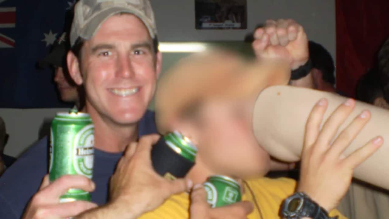 Ben Roberts-Smith smiles as another person drinks from a prosthetic leg.