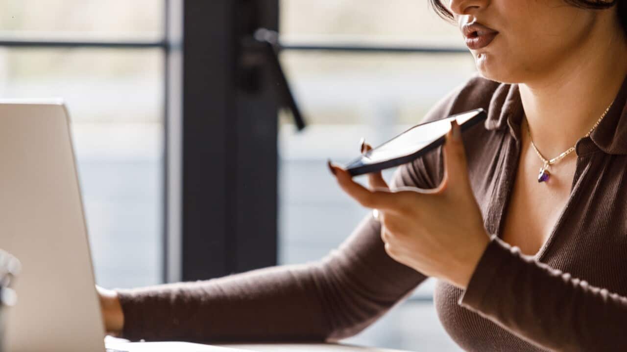 Young woman using laptop and talking on the phone via speakerphone