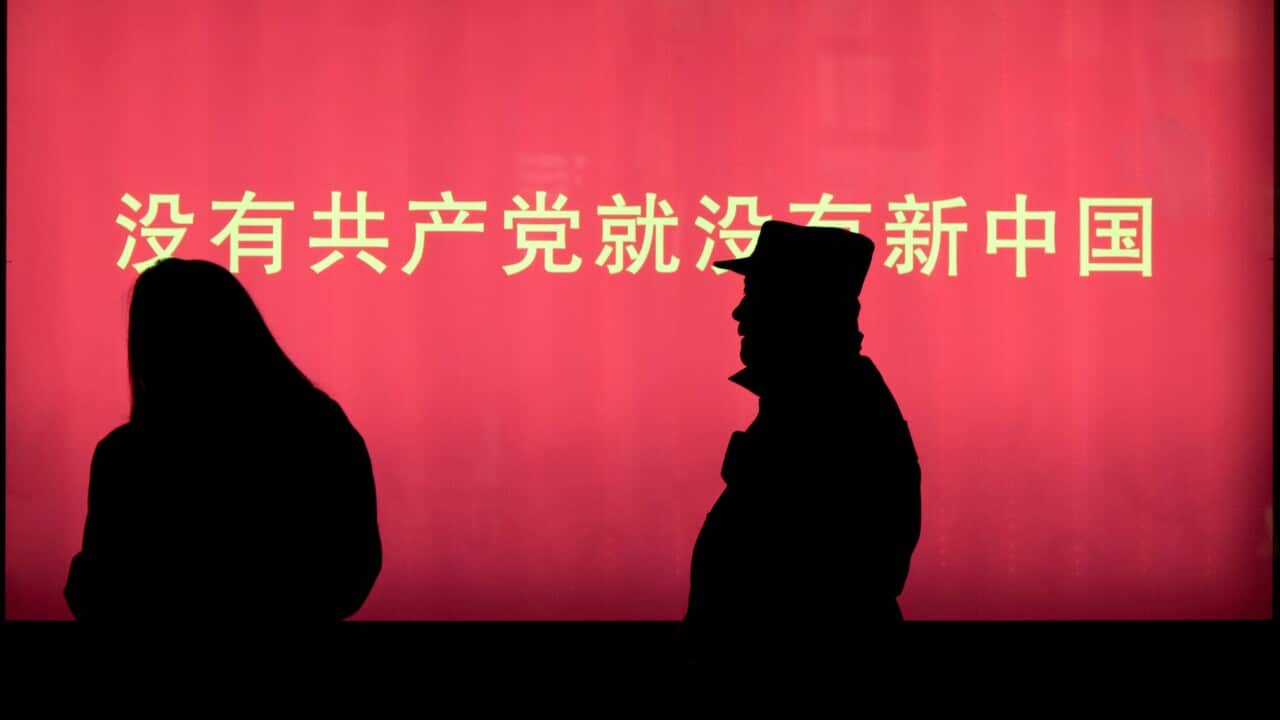 A security person approaches a woman near the slogan "Without the Communist Party,