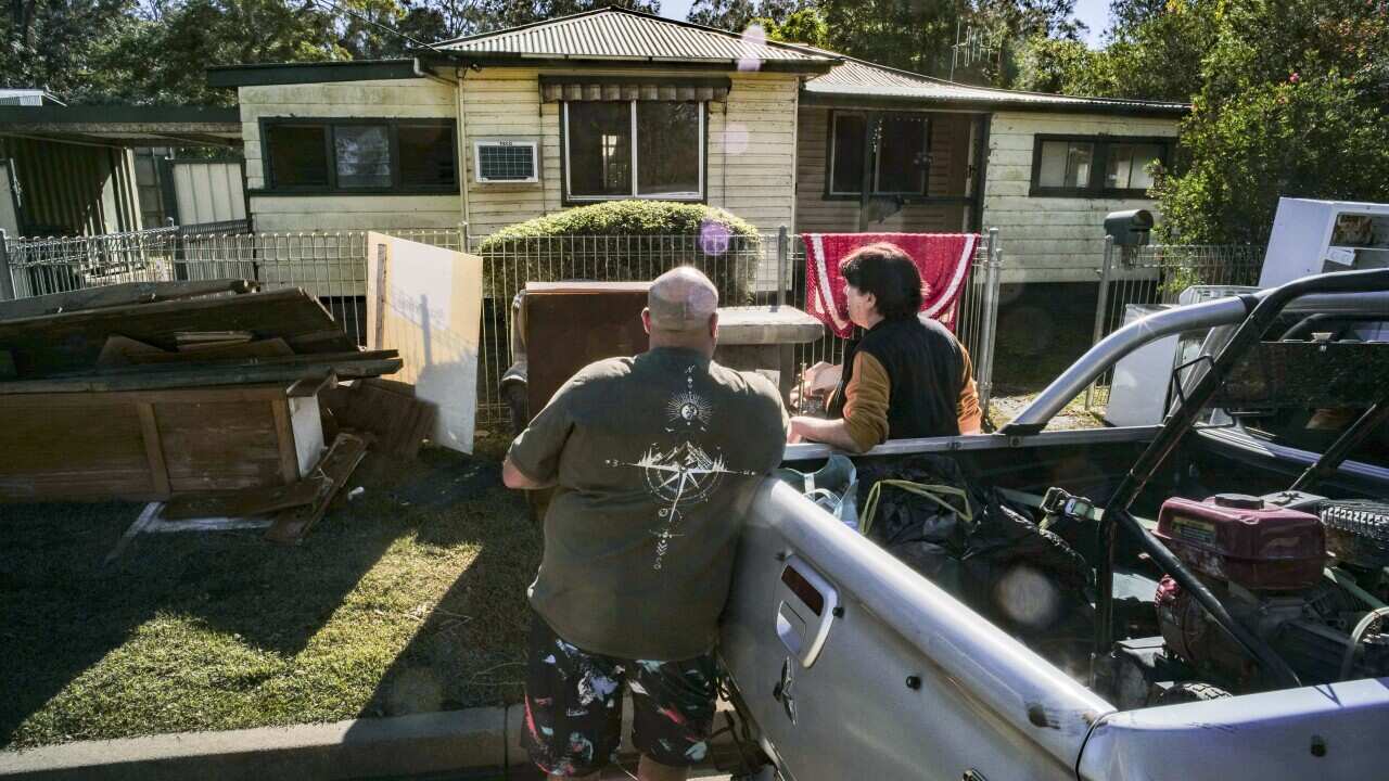 Two people standing next to a ute are assessing the flood damage to their home.