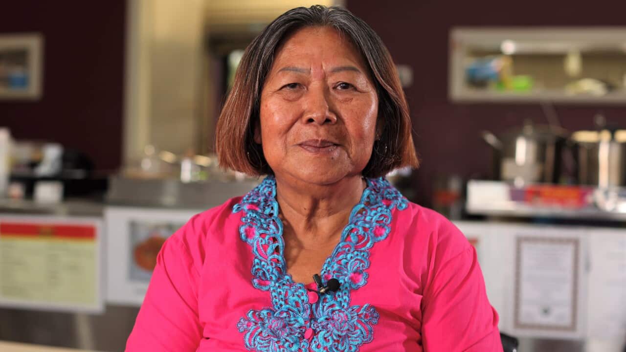 A woman with short brown hair in a pink jacket sits in a cafe smiling at the camera.