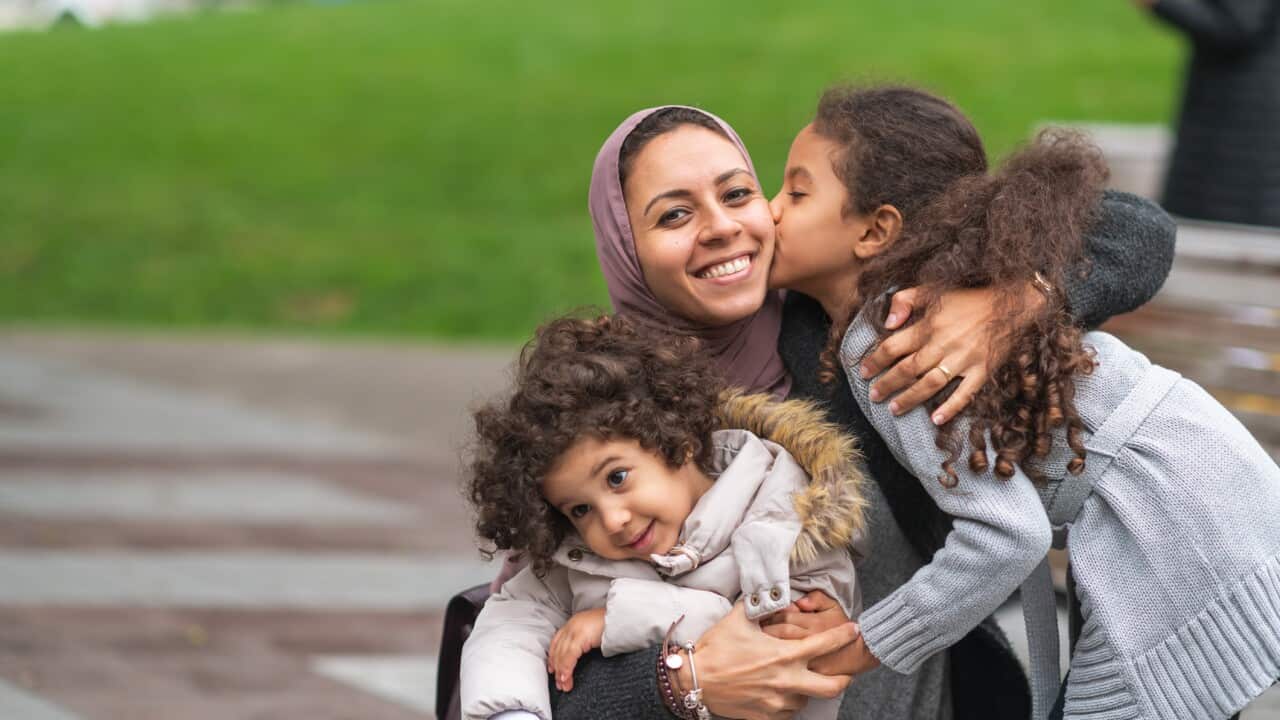 Muslim mother hugging daughters in city park