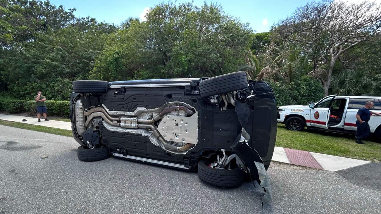 A dark SUV lying completely on its side in the middle of a paved road after an accident.