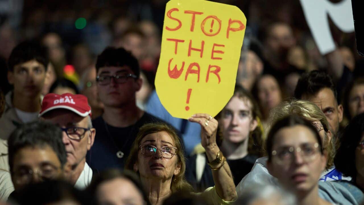 A woman holding a sign saying 'stop the war' in a crowd of people at a protest.