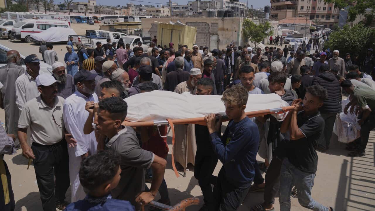 People carry the body of a person covered in a white sheet during a funeral.