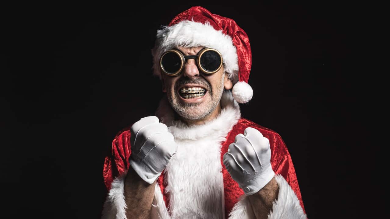 Man dressed as Santa Claus with welder's cyberpunk glasses, opening his mouth and showing his braces, on a black background, clenching his fists. Concept of christmas, celebration, bizarre.