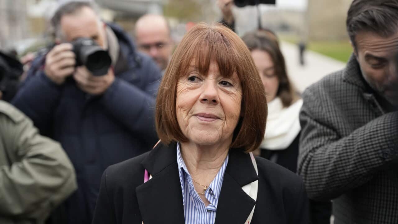 A woman in a black blazer and blue and white striped shirt walking down a street, surrounded by people.