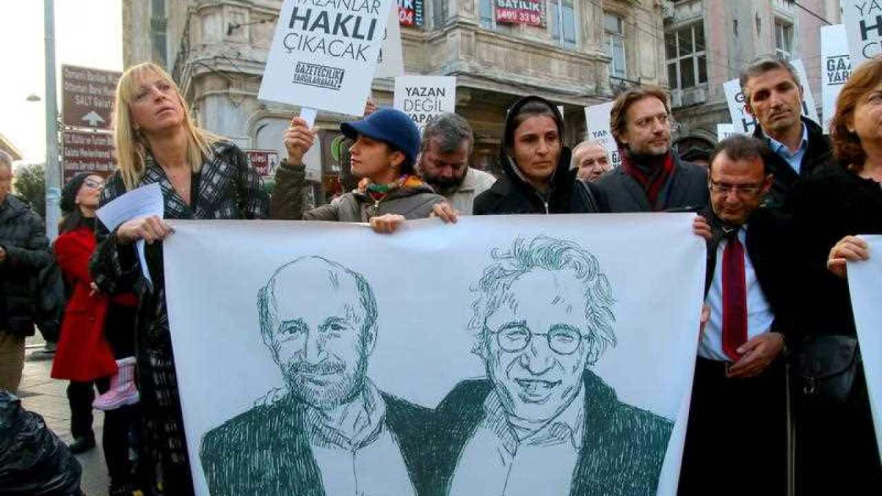 Several people hold a banner showing two drawings of Can Dündar and Erdem Gül as dozens demonstrate in Istanbul