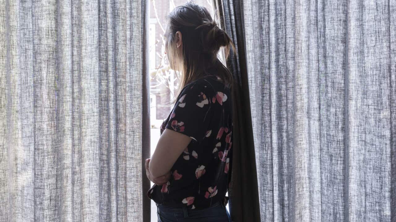A pregnant woman looking out a window, framed by long curtains on either side of her.