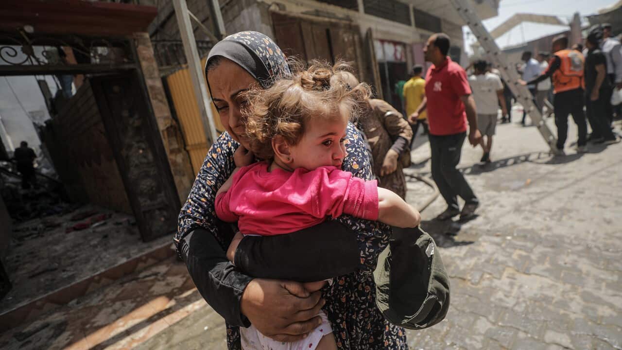 A Palestinian woman holding a child in her arms flees an Israeli airstrike