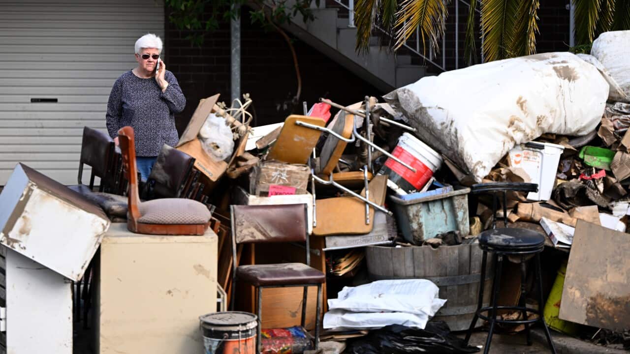 A woman standing outside a home with water-damaged items at the front.