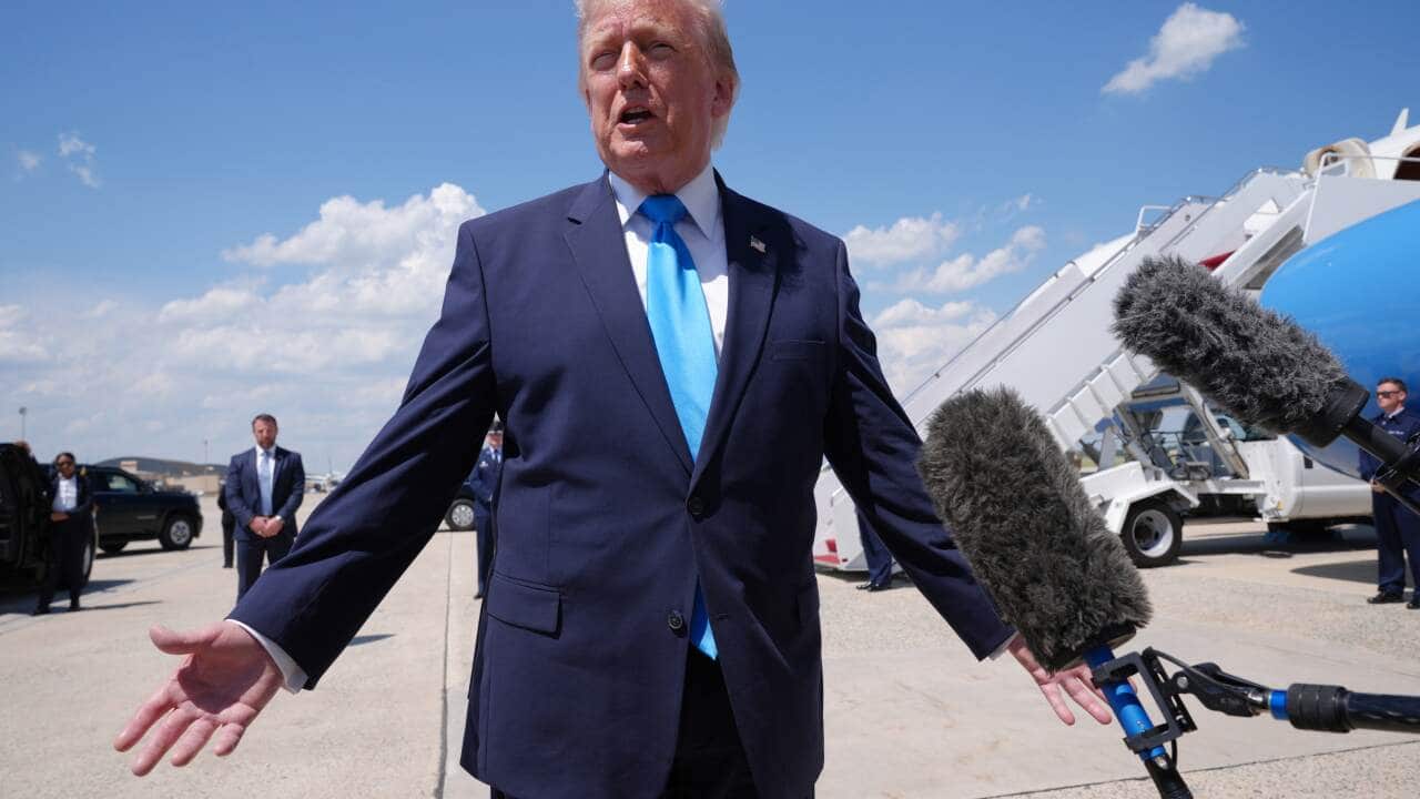 Trump sitting at his desk in the Oval Office at the White House wearing a navy suit and a red tie