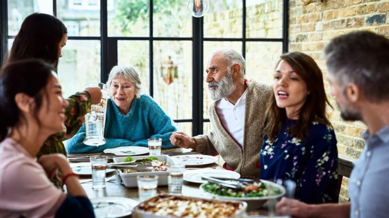 Extended family sitting round dinner table chatting and eating dinner