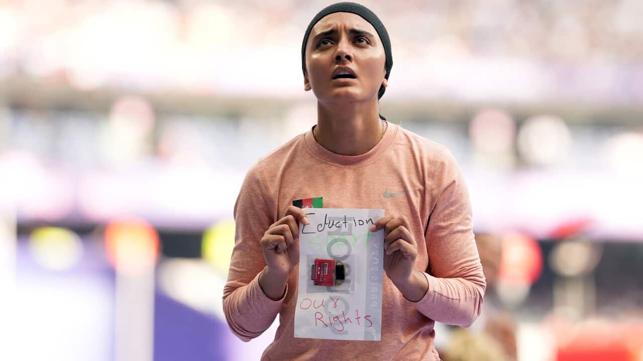A woman in a black head scarf holds up a sign reading 'Education, sport, our rights'