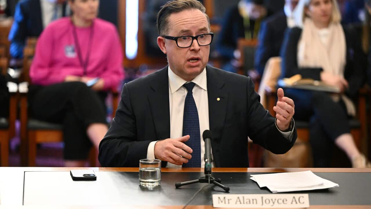 Alan Joyce speaking while sitting at a table in front of a microphone.