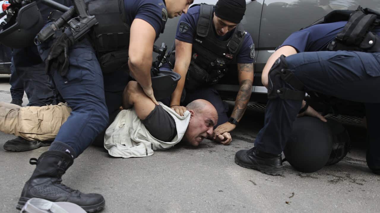 Three armed police officers detain a male protester on the ground