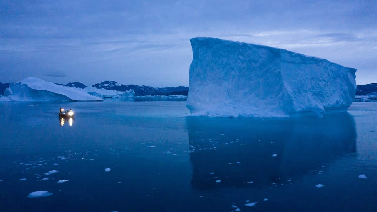 A boat navigates at night next to large icebergs in eastern Greenland. 